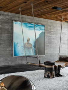 A modern industrial interior featuring a concrete wall, wooden ceiling, and a hanging steel daybed with a serene, underwater-