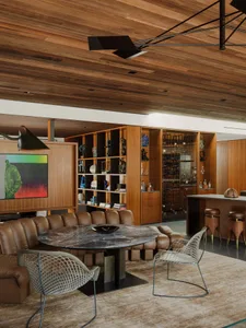 A modern, industrial living room with a round marble table, brown leather furniture, and a wooden ceiling.