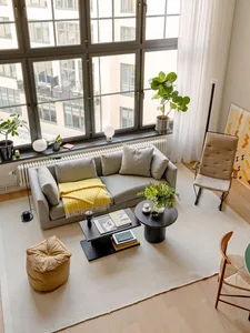 A modern, industrial-style living room featuring a grey sofa, a wooden coffee table, and potted plants.