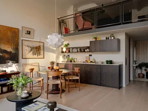 A cozy, industrial-style living room and kitchen with exposed brick walls, wooden furniture, and modern lighting.