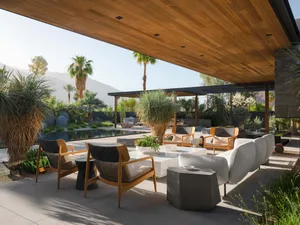 Modern outdoor living space featuring wooden furniture, concrete floor, and glass walls.