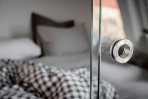 Glass window handle with metal accents in a minimalist bedroom setting.