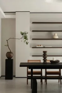 Minimalist dining room featuring a black table, wooden chairs, and ceramic plant pot with greenery.