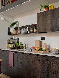 A modern kitchen featuring minimalist design with marble countertops, wooden cabinets, and glassware.