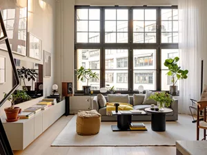 Modern minimalist living room featuring timber furniture, houseplants, and large windows.