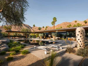 Modern backyard featuring concrete and glass structures surrounded by palm trees and mountains.