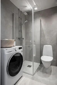 Modern bathroom with concrete walls, glass shower enclosure, washing machine, and toilet.