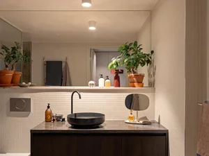 A modern bathroom interior with a black vessel sink, ceramic tiles, green plants, and a dark wooden vanity.