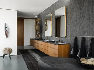 Modern bathroom with wooden vanity, black marble countertop, metallic faucets, and textured grey walls.