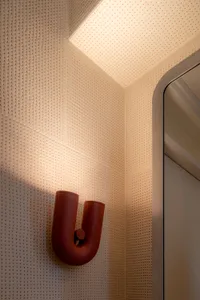 Modern bathroom with metallic red acrylic lighting fixture mounted on textured white wall with circular perforations.