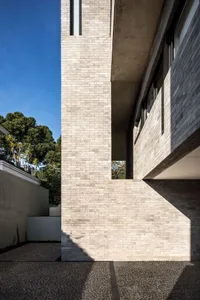 Concrete exterior of a modern house with tall brick wall and glass windows.