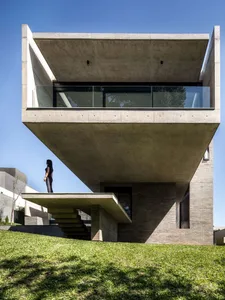A modern house with a cantilevered concrete structure and glass balcony overlooking a green lawn.