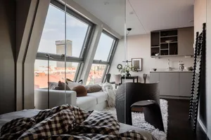 A modern apartment loft featuring a living space with a white sofa, dark furniture, and large windows overlooking the citysca