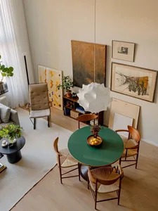 A modern living and dining room featuring wooden furniture and decor with art on the walls and a green table.