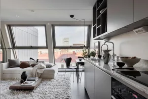 A modern living room with concrete, glass, and metal elements, featuring a white sofa, black chairs, and a minimalist design.