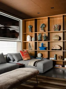 A modern living room featuring wooden shelves, glass sculptures, and metal accents, with a comfortable sofa and a unique rug.