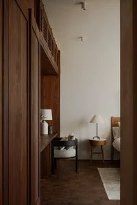 Modern minimalist bedroom with wood furniture, white bedding, and a cozy reading nook.