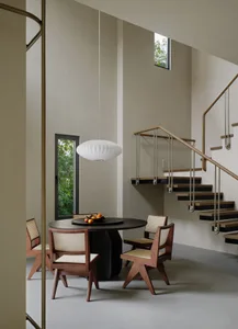 Modern minimalist dining area with a round table, chairs, and a white pendant light hanging above. A staircase with wooden st