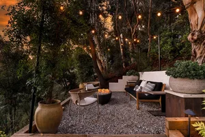 Modern outdoor patio featuring stone and gravel, with comfortable seating and a cozy fire pit under hanging lights.