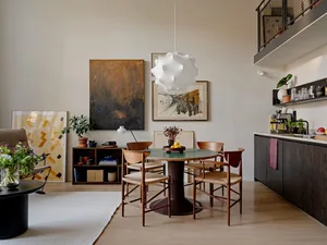 Modern residential dining room with wooden tulip table, metal frame chairs, and abstract art on the wall.