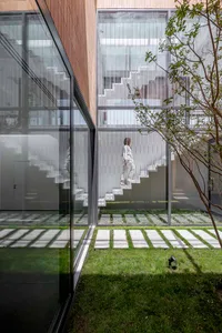 A modern residential building with glass and steel materials, featuring a clear glass courtyard and a person climbing stairs.
