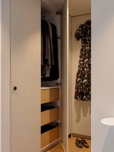 A modern white closet with wooden drawers and a floral dress hanging inside.