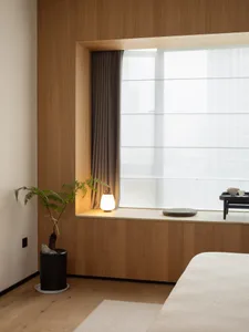 A minimalist bedroom with wooden walls and a cozy reading nook by the window.