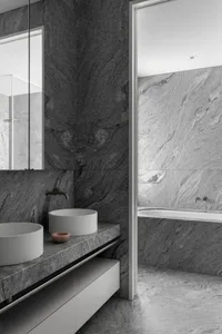 A modern bathroom featuring granite walls and marble sinks.