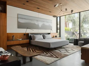 A modern bedroom featuring a bed with a black headboard, grey bedding, and a wooden bench in front of it. The room has a wood