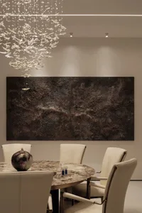 A modern dining room featuring a round table with a marble top, white leather chairs, and abstract art on the wall.