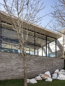 A modern house with a concrete exterior, large glass windows, and rocks in the foreground.