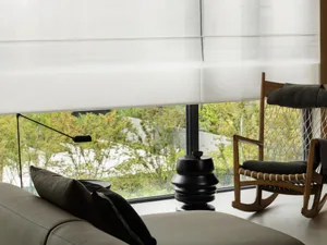 A modern living room featuring a white sofa with black accents, a rocking chair with green cushions, and a black floor lamp. 