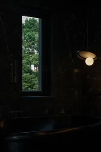 Modern bathroom with black marble walls and a window overlooking green trees.