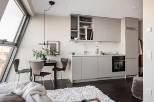 A modern minimalist kitchen dining space featuring a white and grey color palette, sleek furniture, and a large window allowi