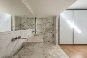 Modern minimalist bathroom with marble walls and floor, featuring sleek, contemporary fixtures.