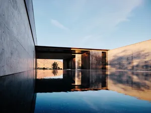 A serene view of a modern poolside with concrete walls reflecting the surrounding mountains.