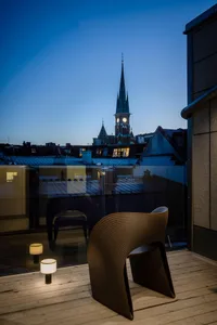 Wooden chair on a deck overlooking a city skyline at dusk, featuring a tall clock tower.