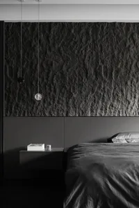 A minimalist bedroom featuring a dark stone accent wall and dark bedding.