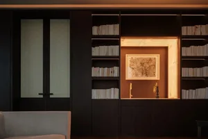 A modern living room featuring dark wood shelves filled with books and a framed abstract painting illuminated by warm lightin