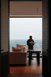 A silhouette of a person standing in a modern interior living room with a large window overlooking a cityscape.