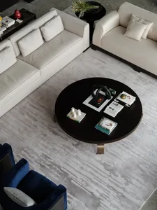 A modern living room featuring a black round table with various items on it, surrounded by light-colored sofas and a dark blu