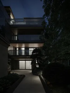 Modern residential building with glass walls, concrete pathways, and metal railings.