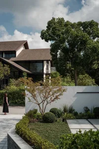 A modern residential home with a concrete exterior surrounded by lush greenery and a clear blue sky with white clouds.