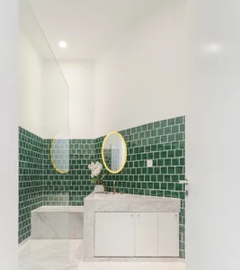 Modern minimalist bathroom featuring green tiles on the walls and a white marble counter.