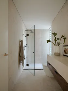 Modern minimalist bathroom with white tiled walls, floor, and ceiling, featuring a walk-in shower with glass door, a wall-mou