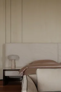 A minimalist bedroom featuring a beige upholstered bed with marble nightstand and beige fabric bedding.