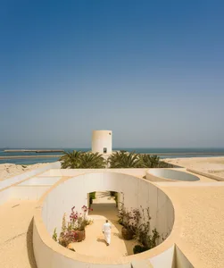 A modern architectural development with a white facade, featuring a circular courtyard with plants and a man walking.