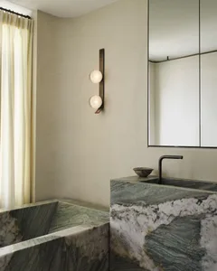 Modern bathroom featuring a white marble tub and sink with black fixtures, illuminated by a wall-mounted light fixture with t