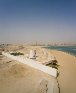 Modern beach-front property with a cylindrical concrete structure on a sandy beach.