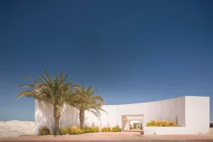 A modern building with a white, curved concrete exterior and palm trees in front of it.